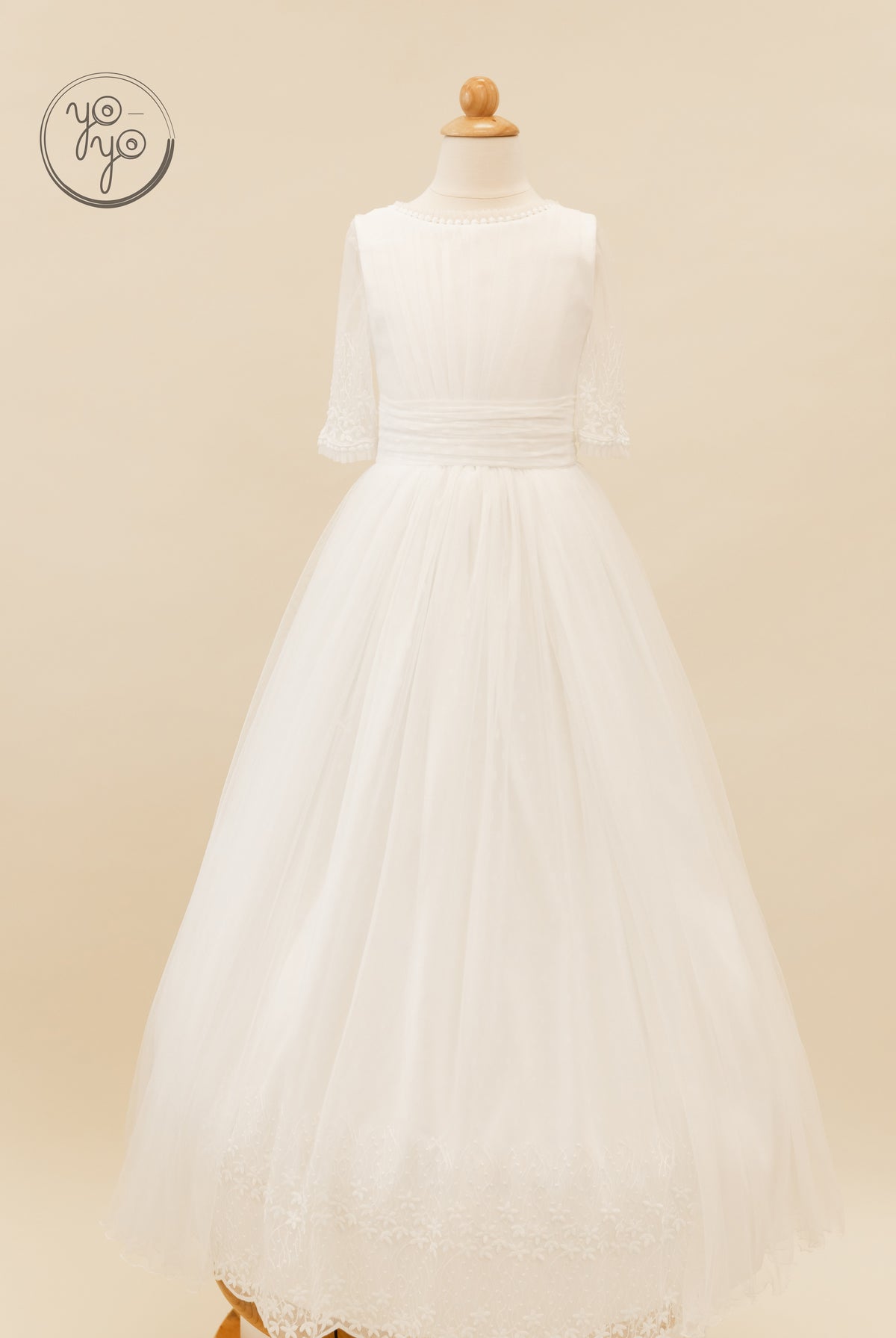 White Hibisco dress on a mannequin featuring three-quarter lace sleeves, a pleated bodice, and a French tulle skirt with a scalloped hem.