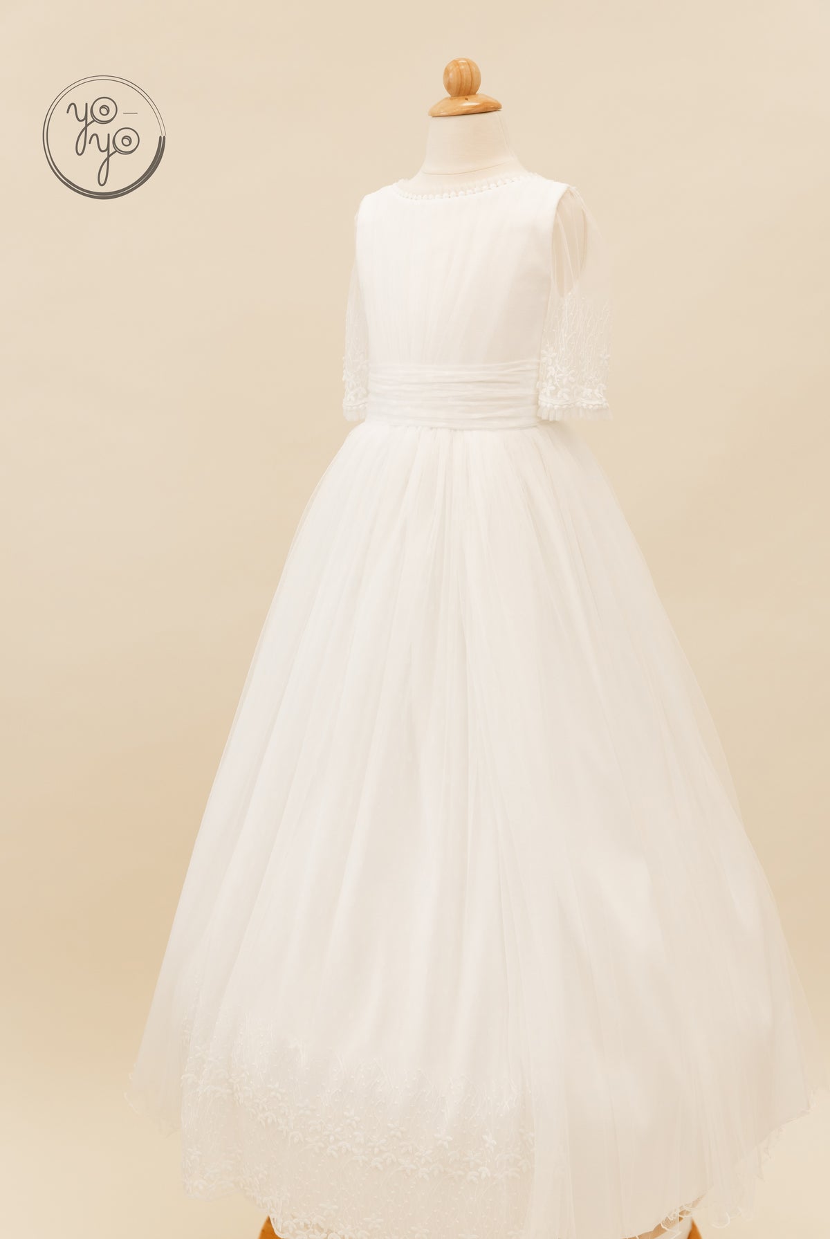White Hibisco floor-length dress by YoYo Boutique on a mannequin, featuring sheer sleeves, a pleated waist, and lace trim at the neck and hem.