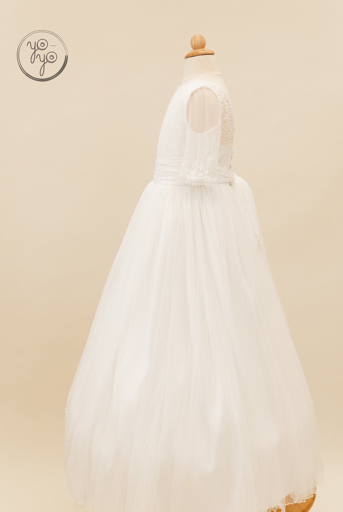 Side view of the white Hibisco Dress with sheer sleeves, a floral lace bodice, and a tulle skirt with a waist ribbon.
