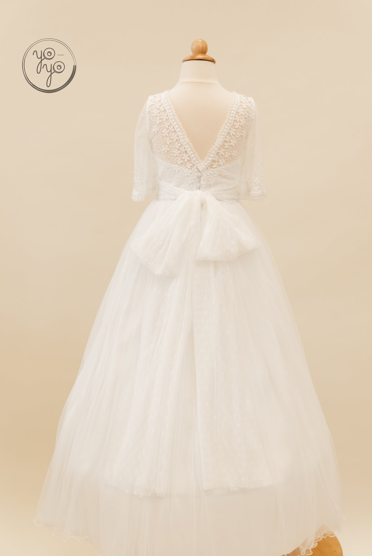 Back view of the white Hibisco Dress by YoYo Boutique, featuring a lace bodice, V-neck, elbow-length sleeves, a waist bow, and a French tulle skirt.