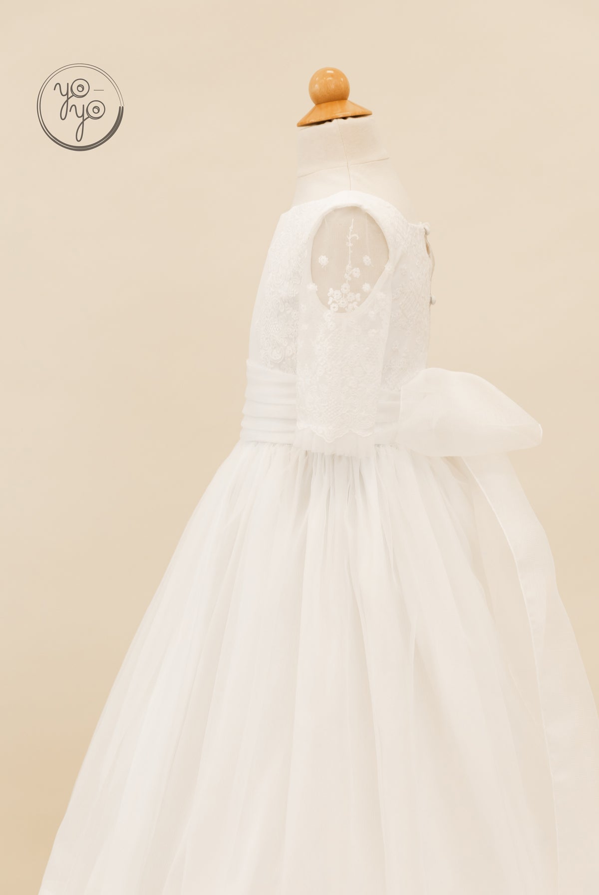Side view of a white, boho-style Gladiola Dress by YoYo Boutique on a mannequin, featuring lace sleeves and a large waist bow.
