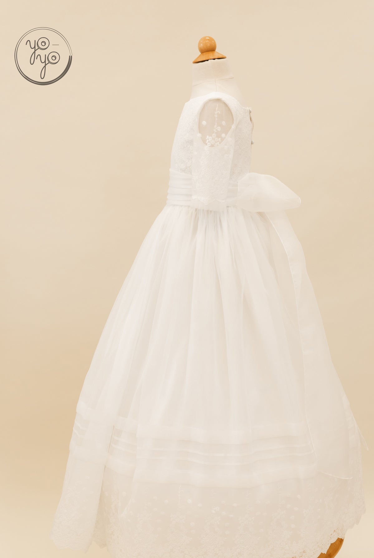 YoYo Boutique Gladiola dress on a mannequin with white lace sleeves, a waist sash with a back bow, and a floor-length tulle skirt.