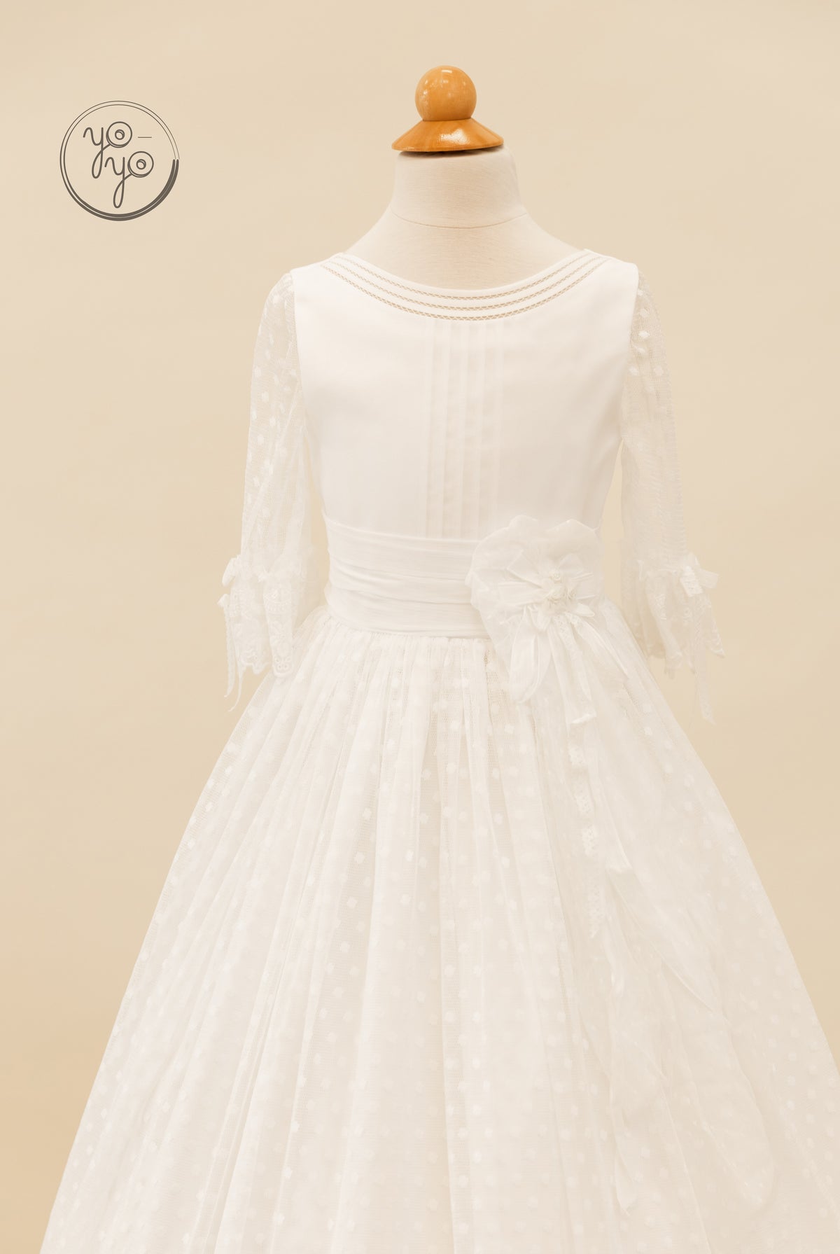 The white knee-length Cassia Dress by YoYo Boutique features a round neck, three-quarter lace sleeves, and a floral waist sash.