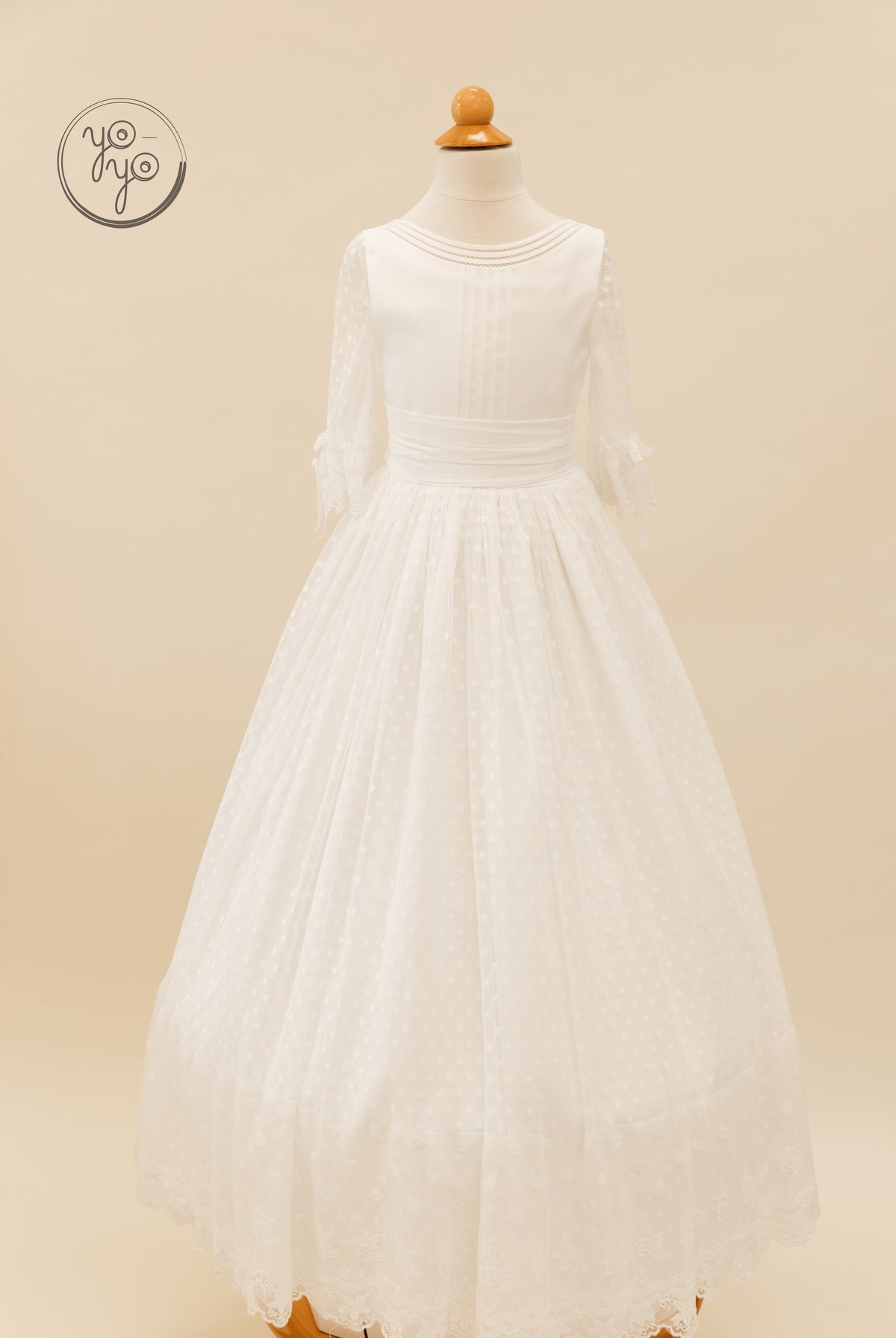 YoYo Boutique Cassia white floor-length Communion dress featuring a pleated bodice, sheer Swiss dot sleeves, and a lace-trimmed hem.