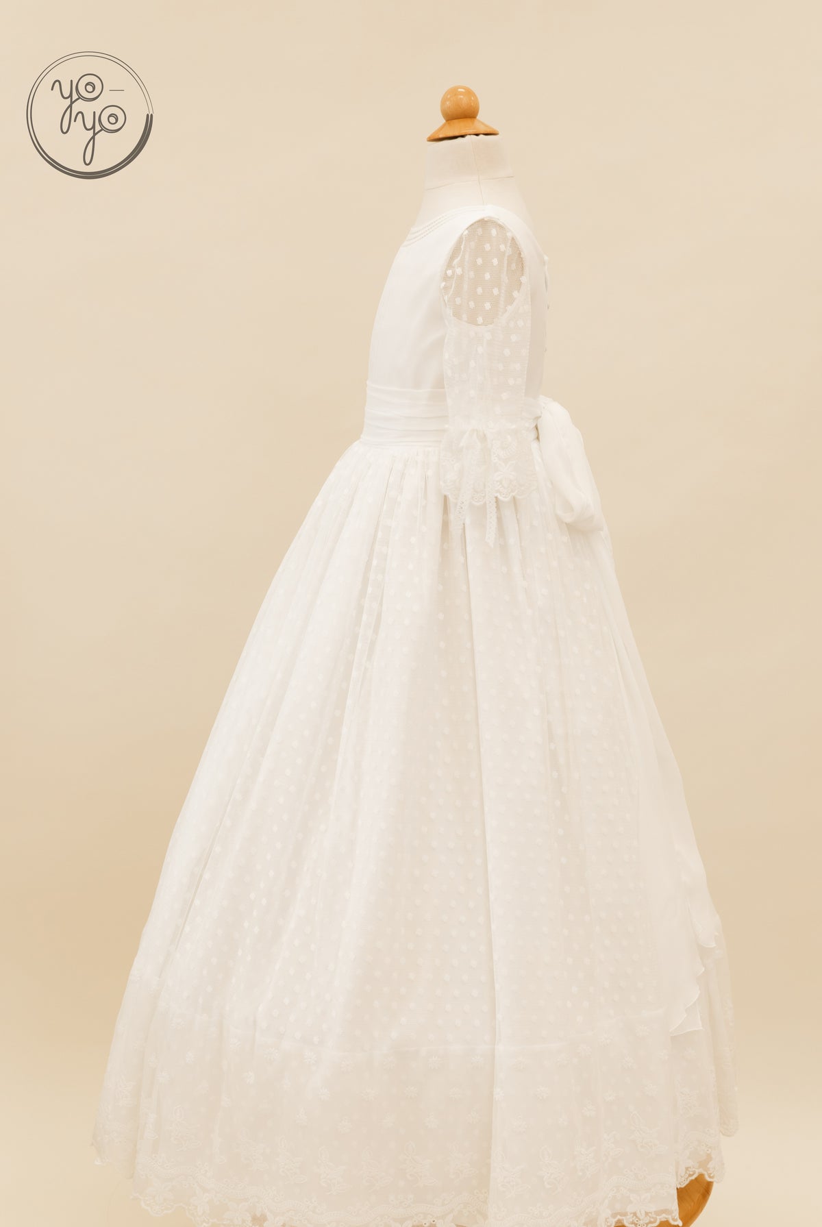 Cassia Dress by YoYo Boutique: floor-length white boho Communion dress with sheer polka dot sleeves, lace hem, and tie-back waist.