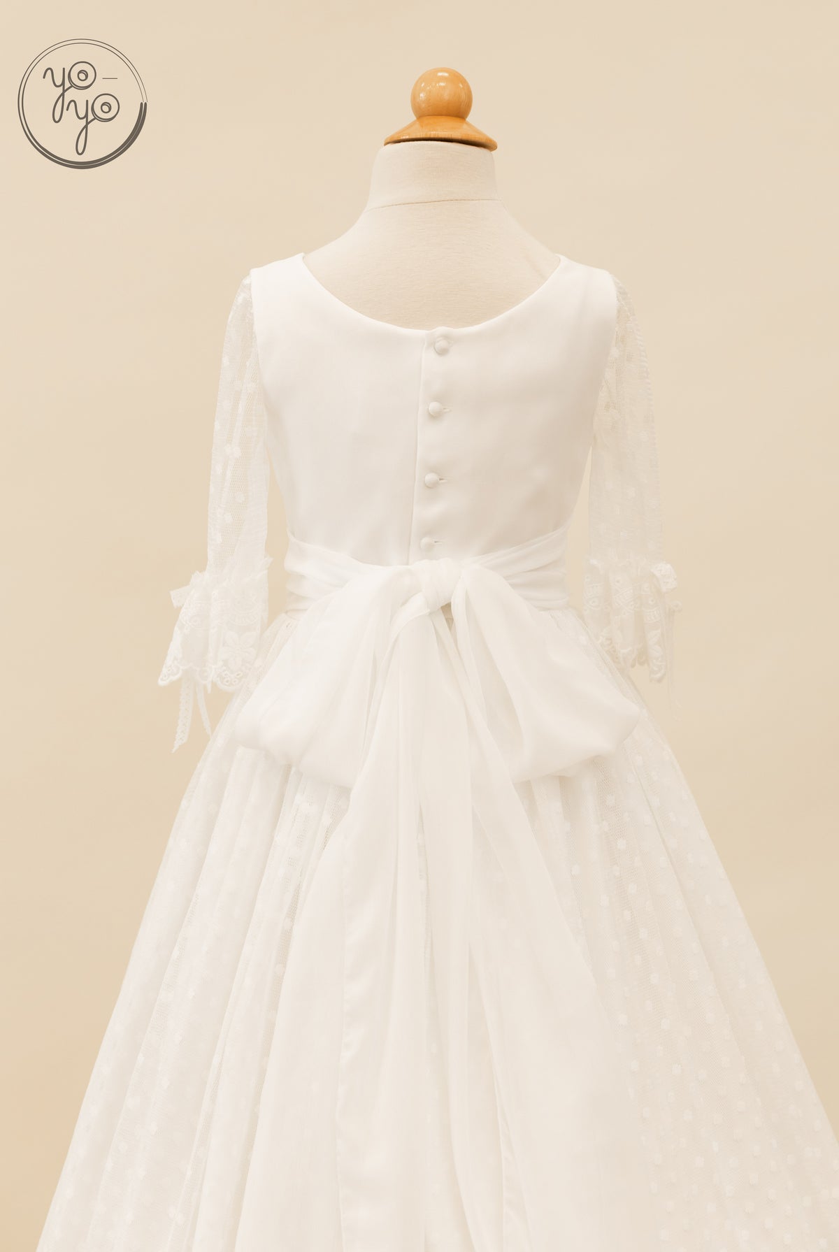 Back view of the Cassia boho First Communion dress, featuring sheer lace-trimmed three-quarter sleeves, a button-up back, and a large waist bow.