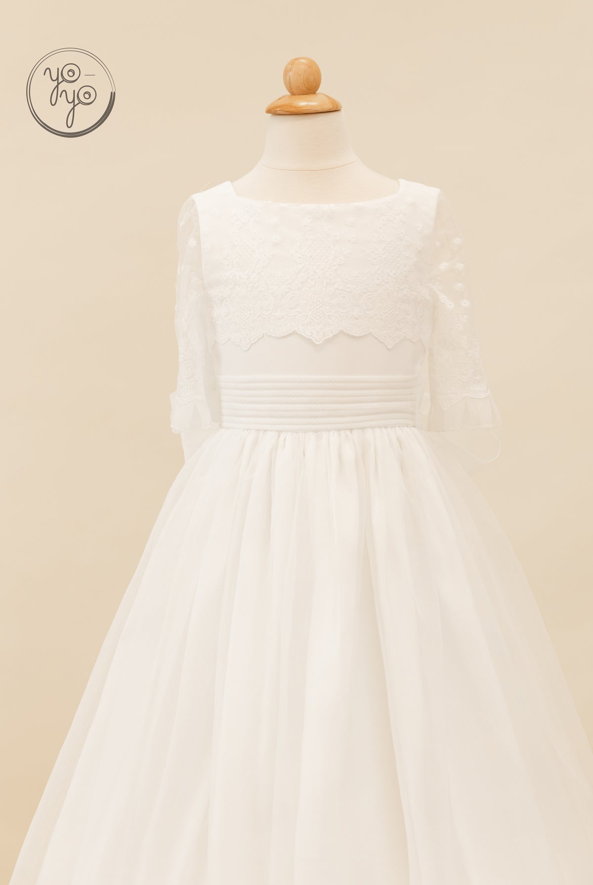 White Campanilla dress on a mannequin, featuring an embroidered floral lace bodice, three-quarter sleeves, pleated waistband, and full tulle skirt.
