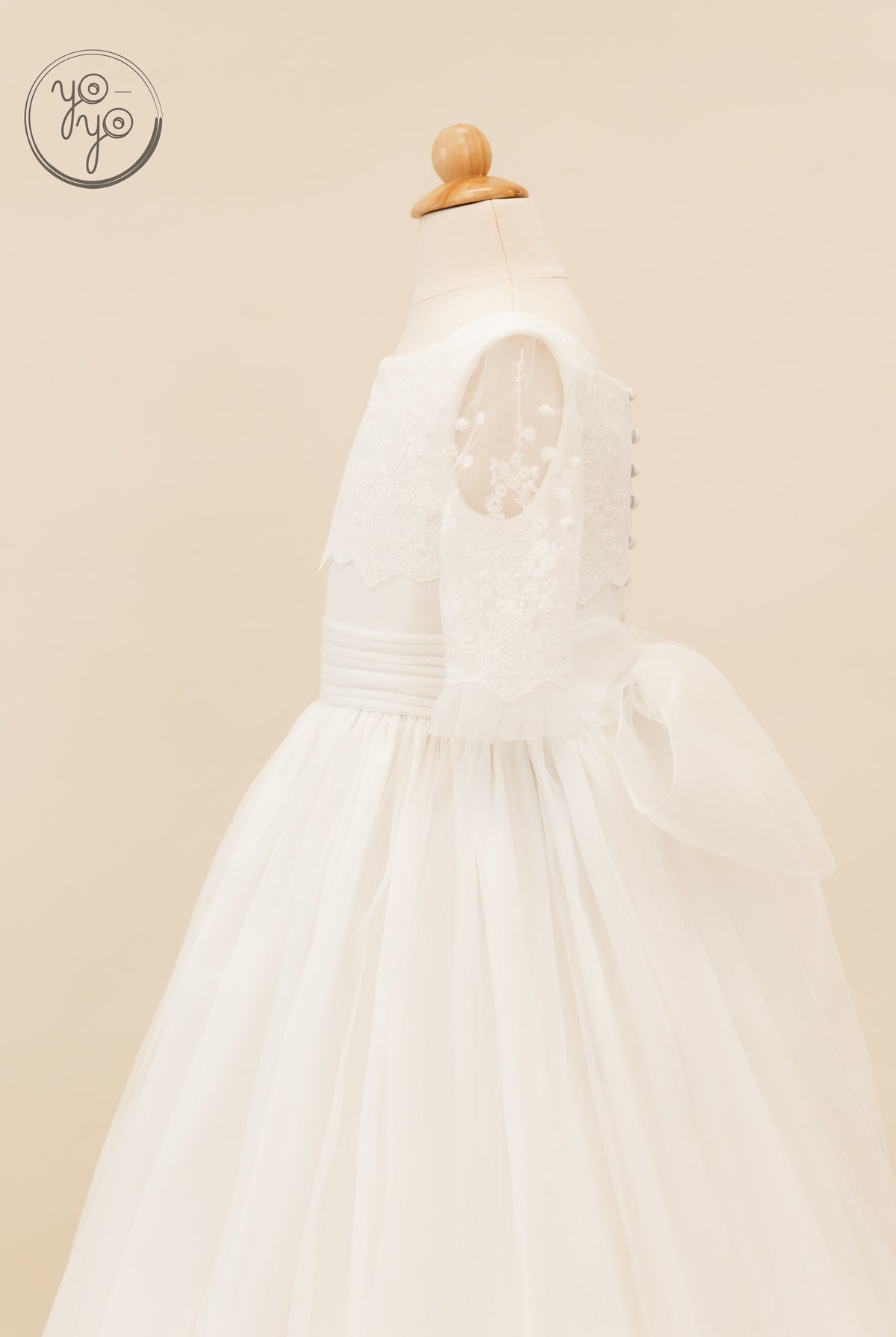 White Campanilla dress featuring a lace bodice, sheer floral sleeves, a wide waistband, and a large back bow.