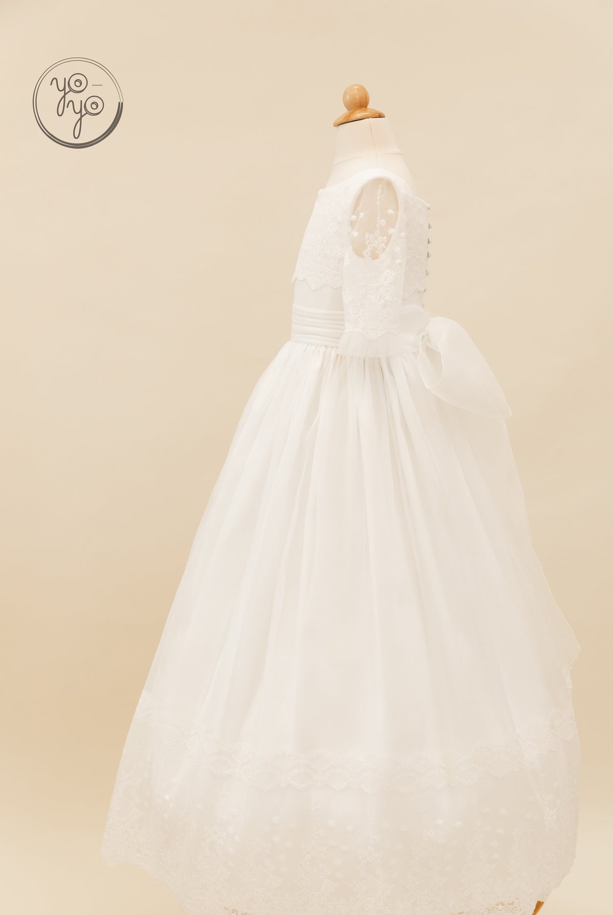 Side view of the white, boho Campanilla Dress by YoYo Boutique with short lace sleeves, a wide waistband, and a large back bow.