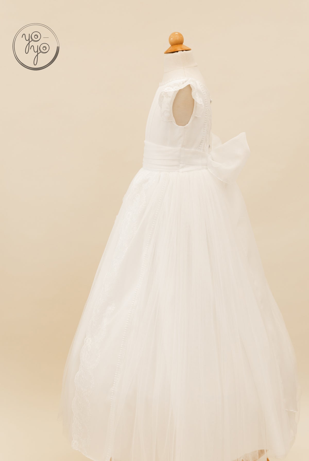 Side view of the white lace Buganvilla Dress by YoYo Boutique, featuring a sleeveless bodice, tulle skirt, and a large bow at the back waist.