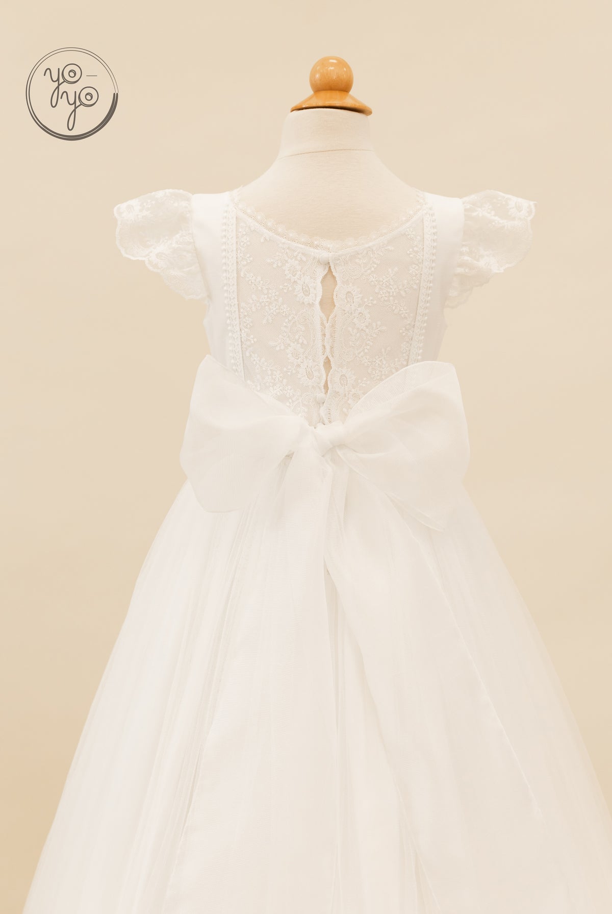 Back view of the white lace Buganvilla Dress featuring scalloped cap sleeves and a large organza bow at the waist.