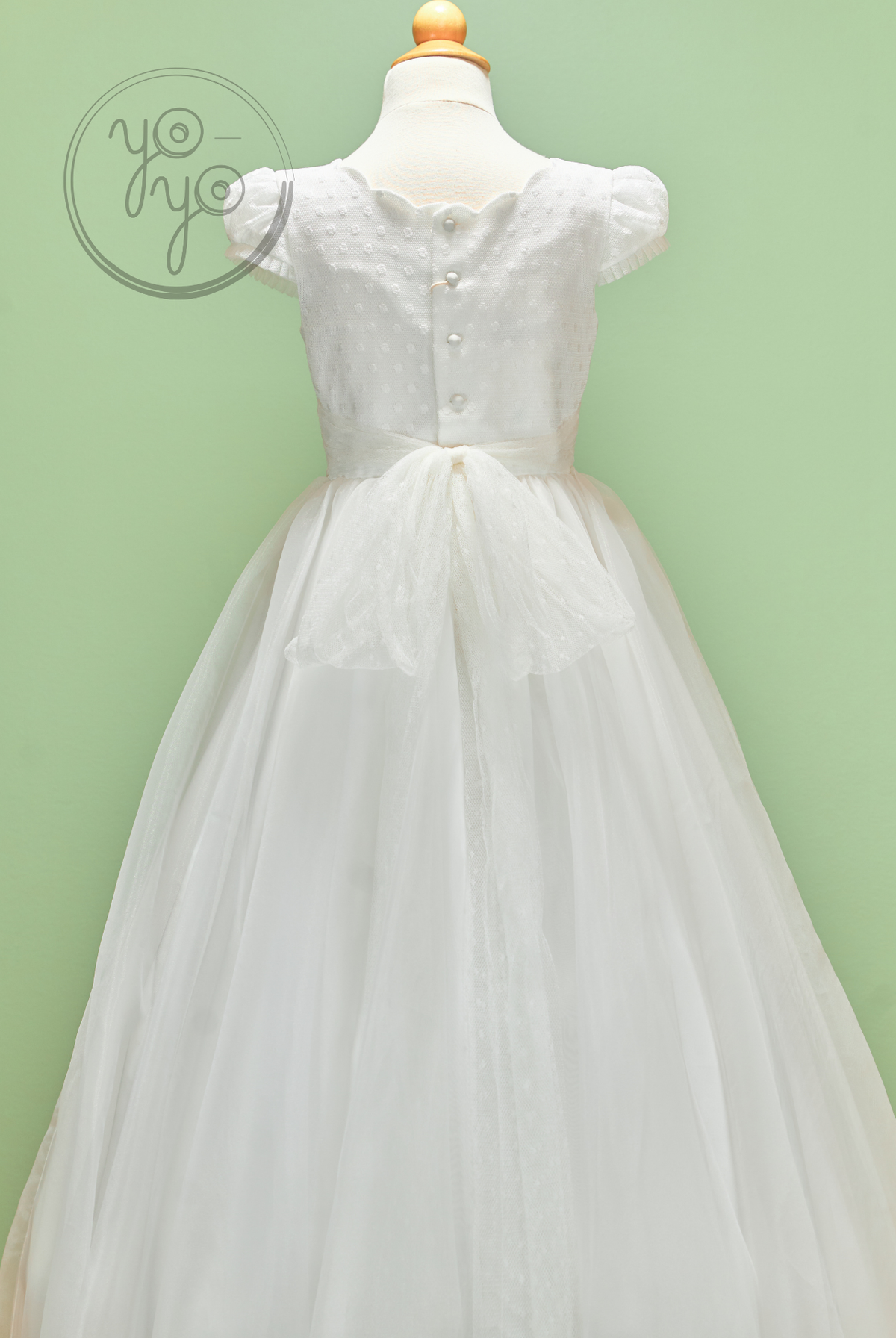 Back view of the white, embroidered tulle Iris Dress by YoYo Boutique, featuring a dotted bodice, button-up back, and sheer waist bow.