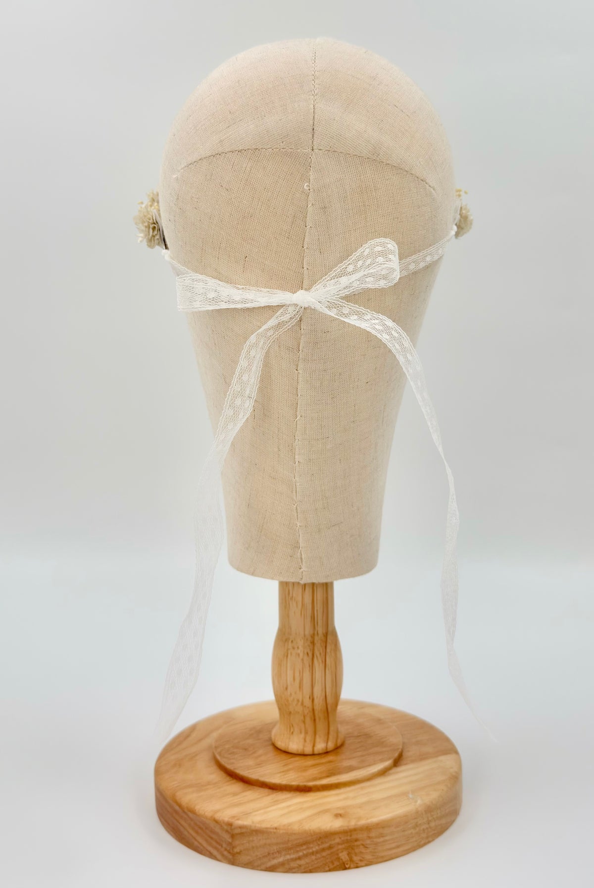 Back view of the Off-White Flower Headpiece on a mannequin, featuring small cream flowers and a thin white lace ribbon bow.